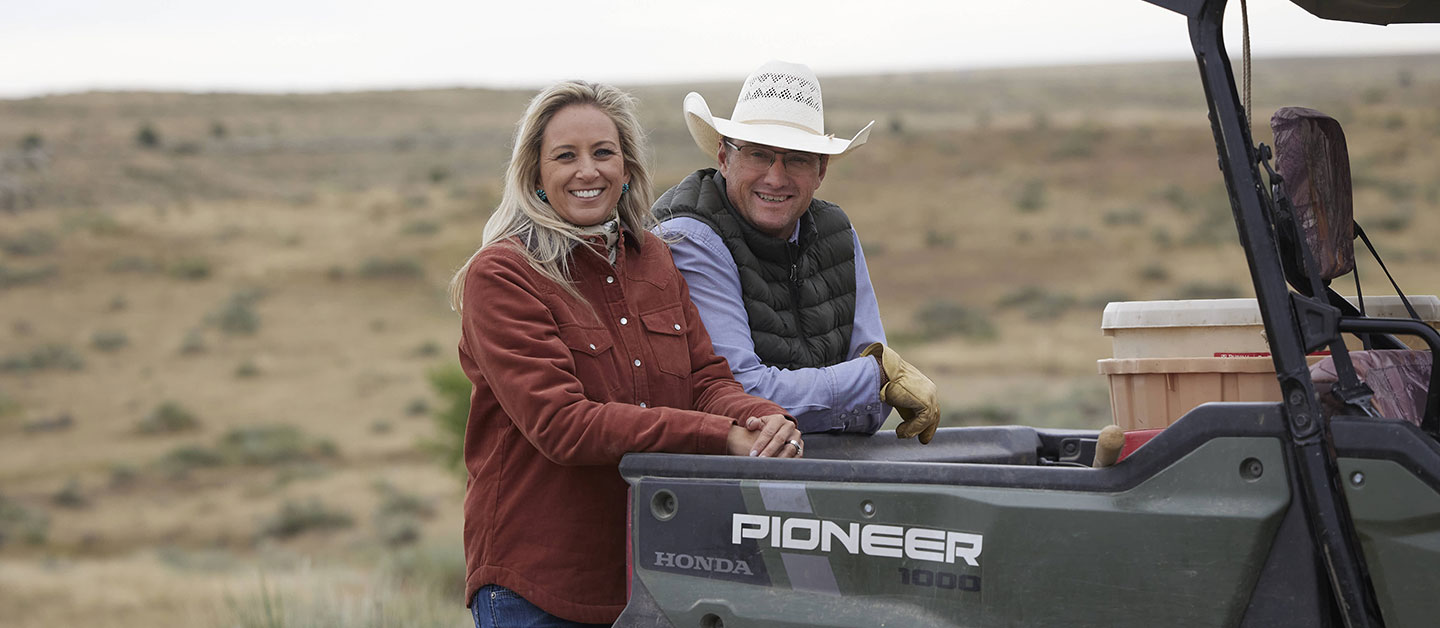 Shali & her husband posing for the camera leaning up against a pioneer four by four.